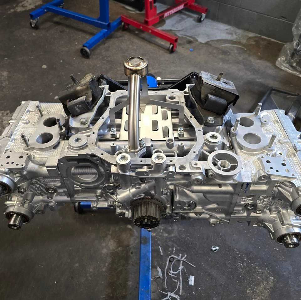 Engine block, disassembled and partially reassembled, lying on a work surface. Metal components are silver, with some blue and black accents.