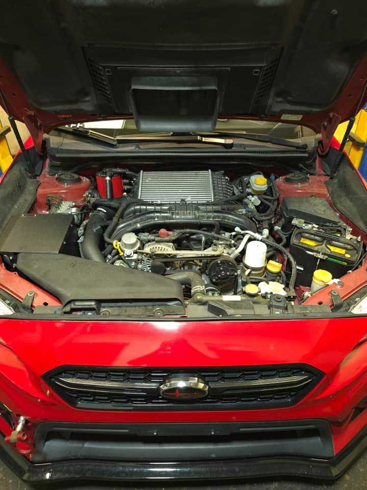 Red car engine bay with opened hood; modified engine components visible.
