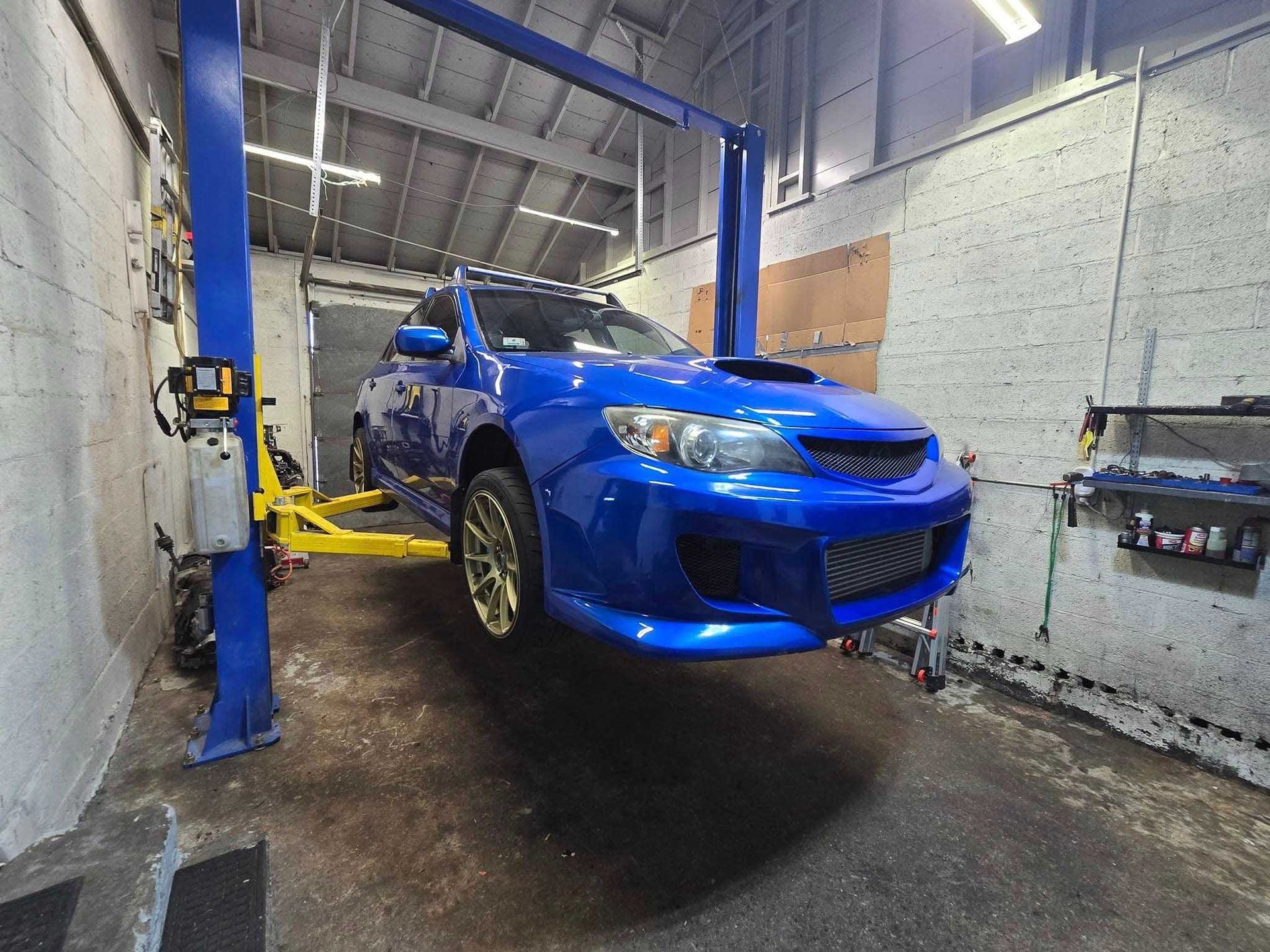 Blue car lifted on a yellow car lift in a garage.