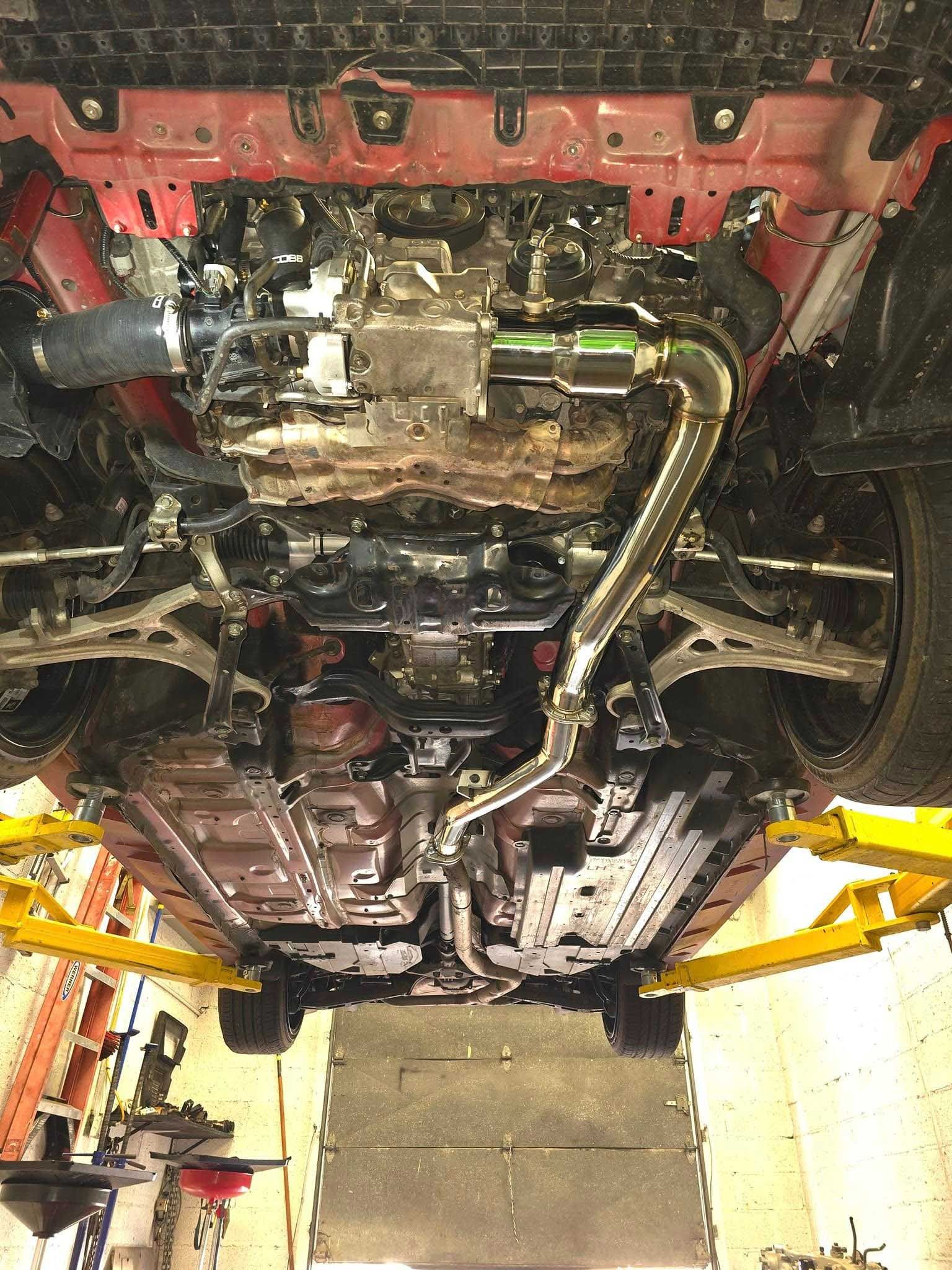 Underside view of a red car lifted on a hoist, revealing exhaust and undercarriage components.