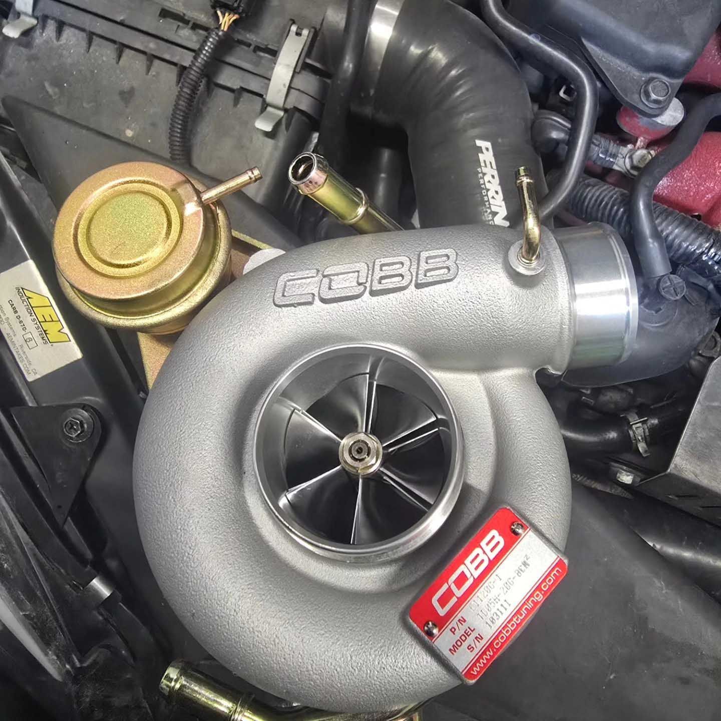 Silver Cobb turbocharger with open impeller sits on a car engine.
