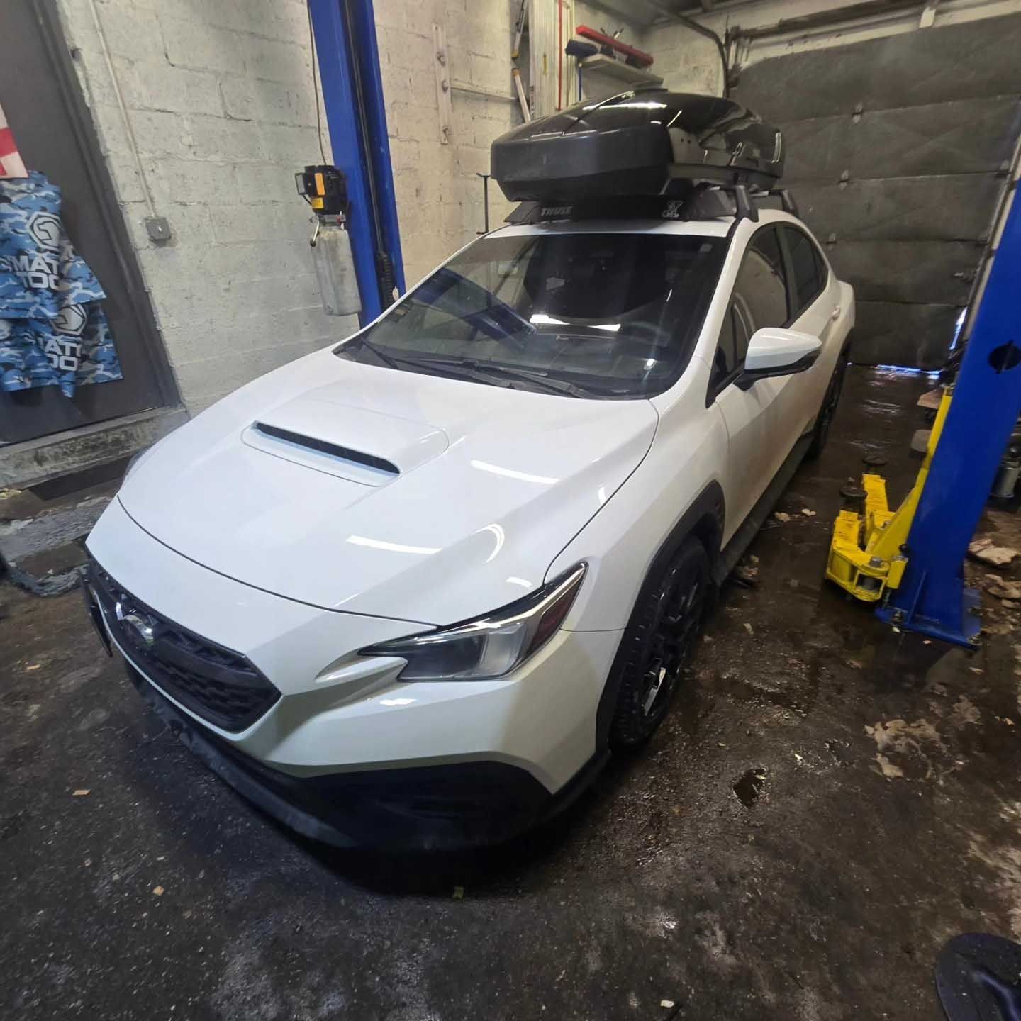 White Subaru WRX with black roof rack in a garage.
