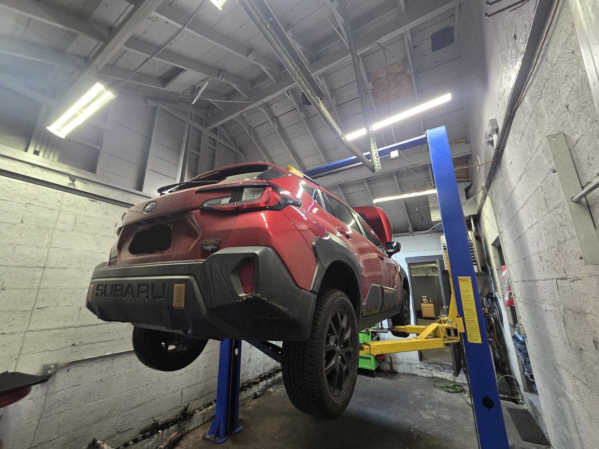 Red Subaru SUV on a hydraulic lift in a garage.