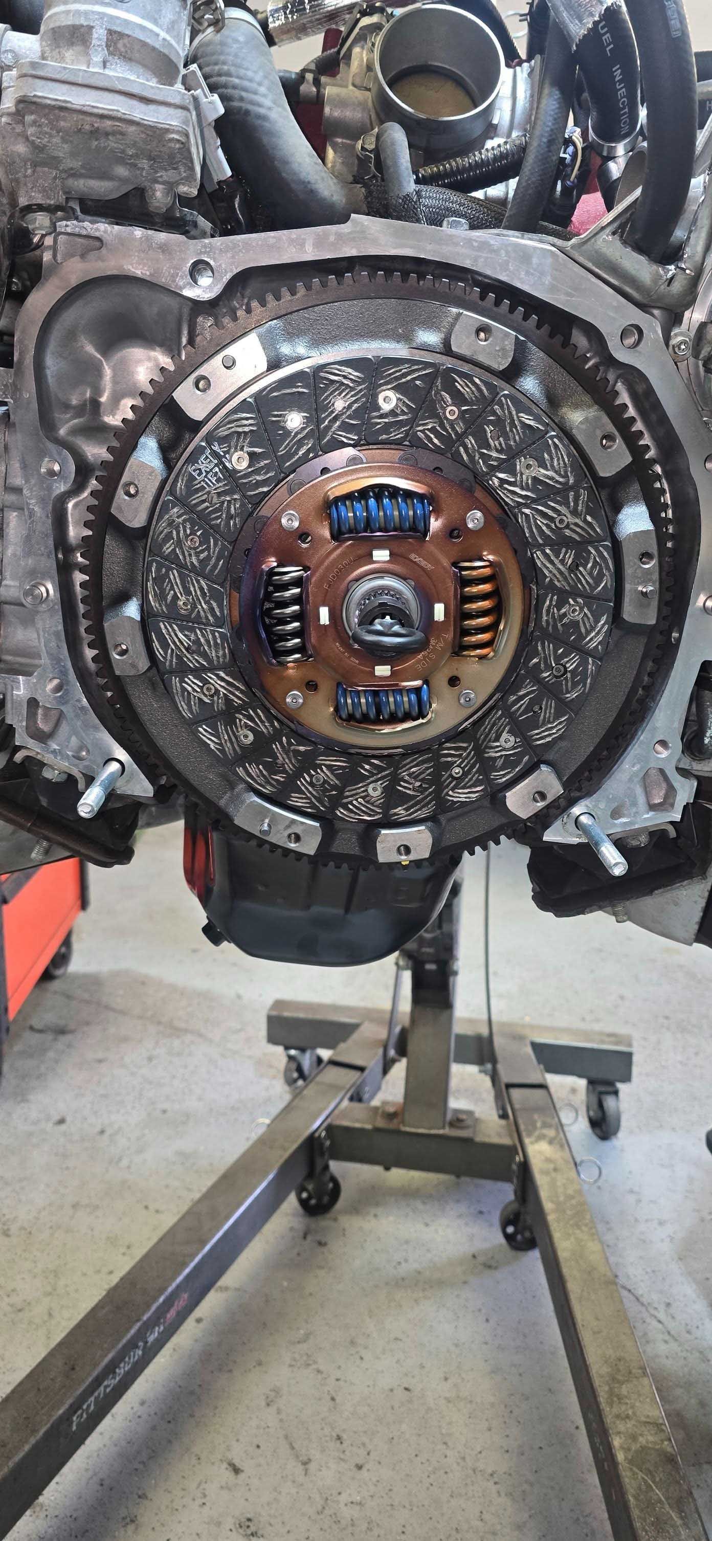 Engine with clutch assembly attached, mounted on a stand in a workshop.