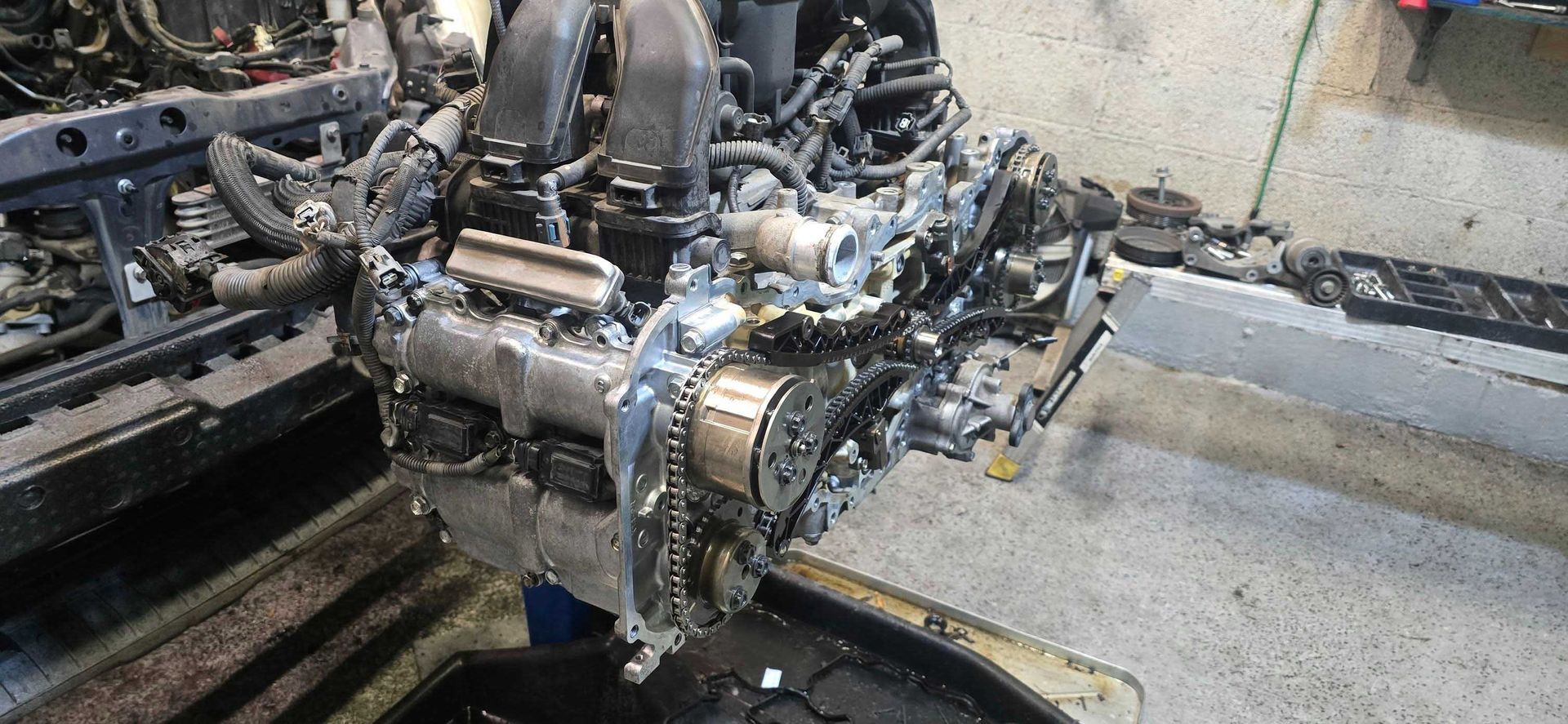 Car engine, partially disassembled, showing internal components. Workshop setting with metal frame visible.