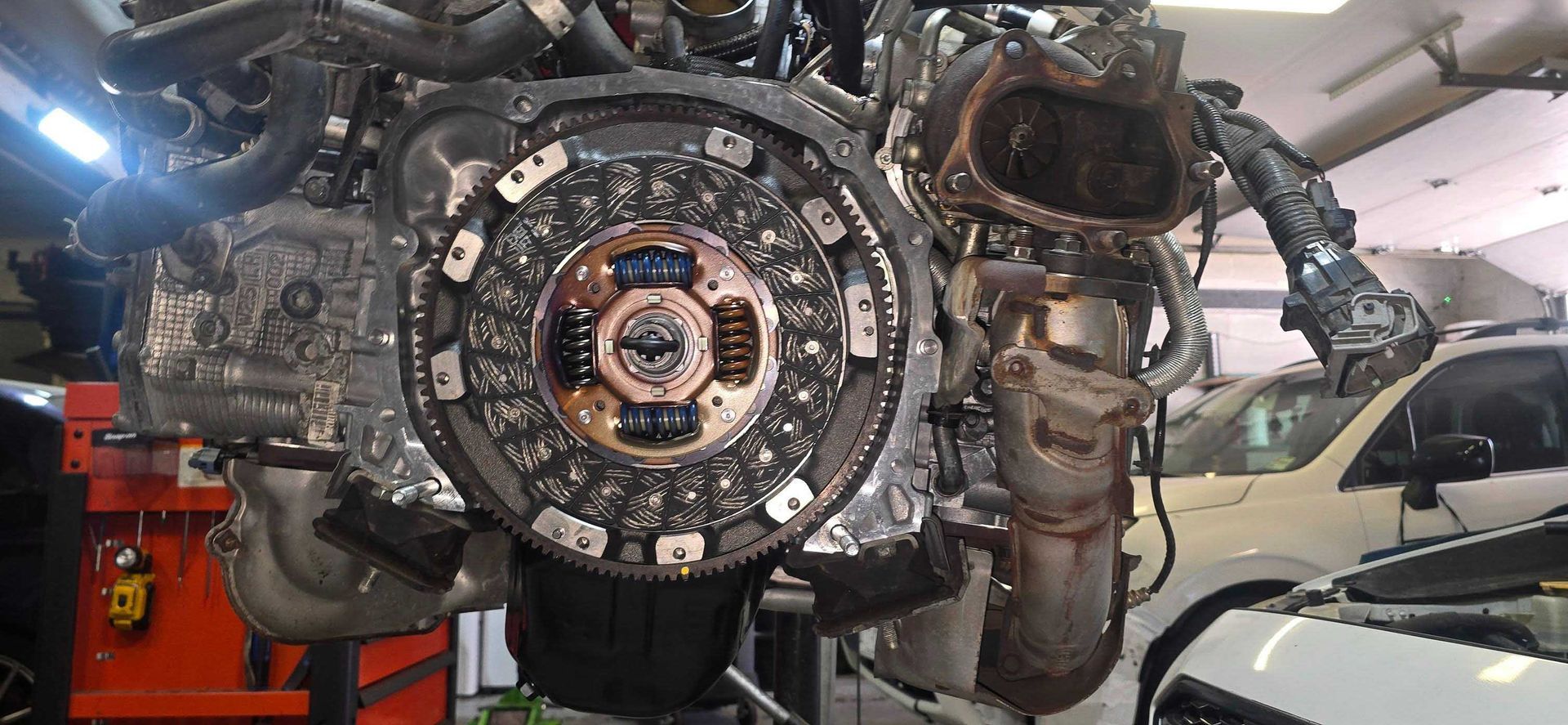 An engine with a clutch visible. The engine is in a repair shop.