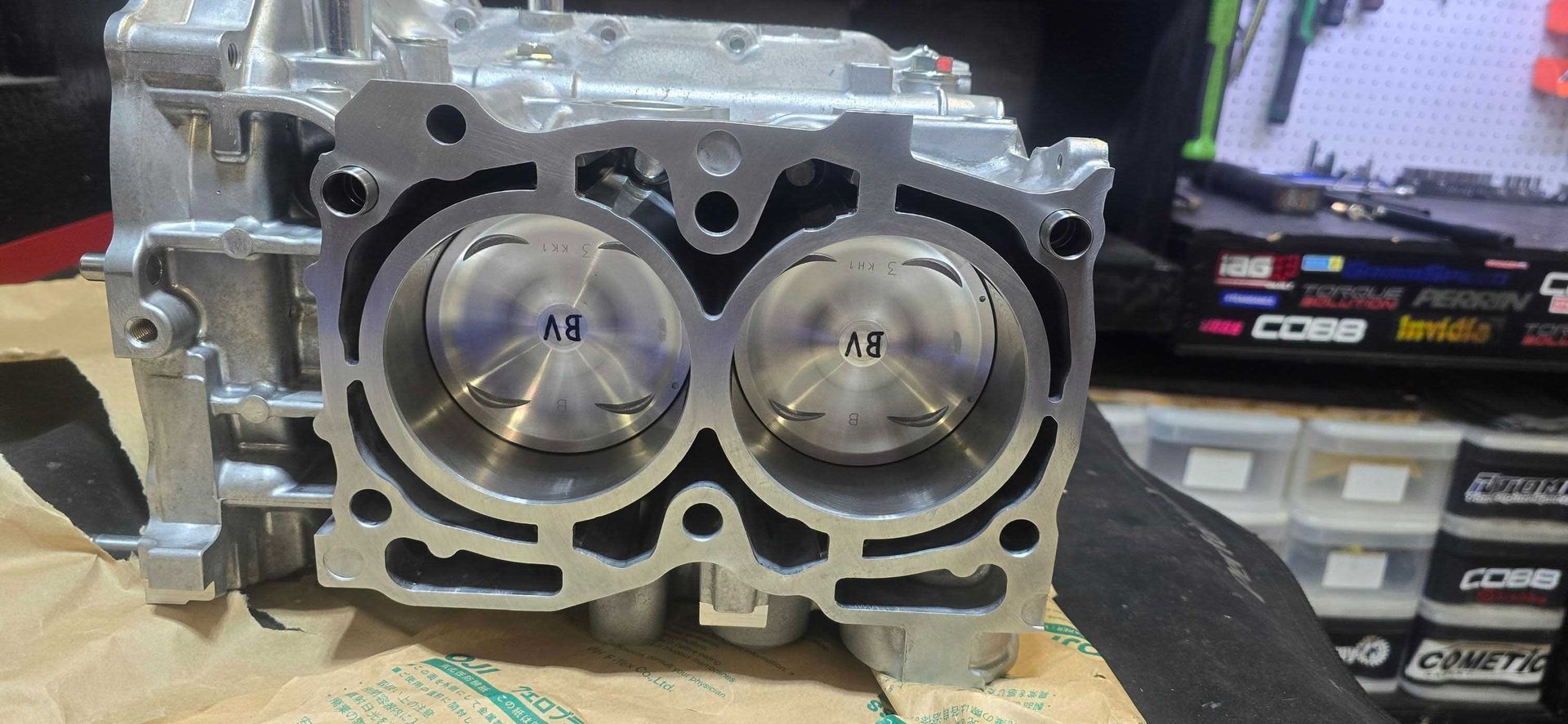 Engine cylinder heads with pistons visible. Close-up shot with two visible cylinders, metal, and light reflections.