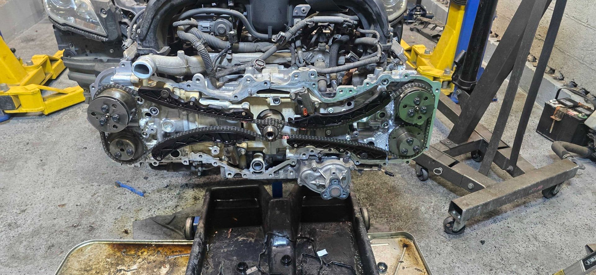 Car engine being worked on in a garage. Parts are exposed and oily, supported by stands.