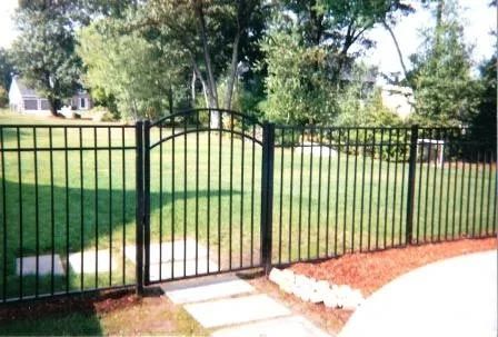 A black fence with a gate in the middle of a lush green field.