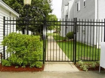 A black metal fence surrounds a walkway leading to a house.