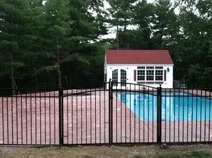 A fence surrounds a swimming pool with a white house in the background.