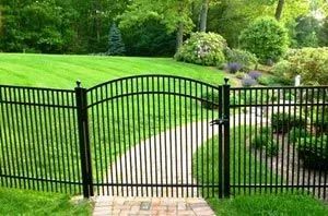 A black fence surrounds a path leading to a lush green field.