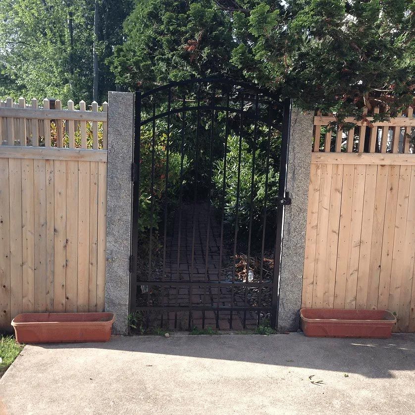 A wooden fence with a metal gate leading to a garden