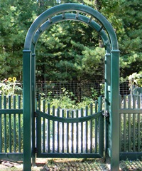A green gate with a fence behind it and trees in the background