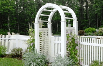 A white arch is surrounded by a white picket fence