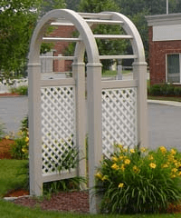 A white arch with a lattice behind it is in a garden.