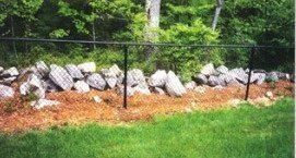 A stone wall with a chain link fence surrounding it.