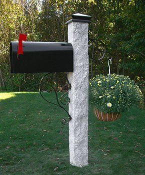 A black mailbox is sitting on top of a white stone post.