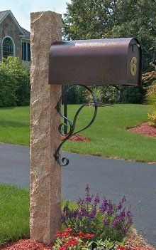 A mailbox is sitting on top of a stone post in front of a house.