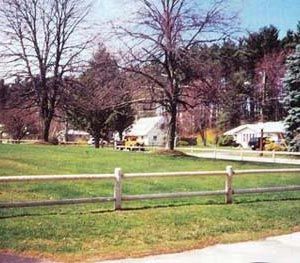 A wooden fence surrounds a grassy field with trees in the background