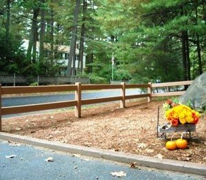 A wooden fence with pumpkins and flowers in front of it