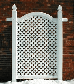 A white lattice fence is sitting in front of a brick wall.