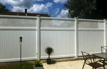 A white fence surrounds a patio with a table and chairs.