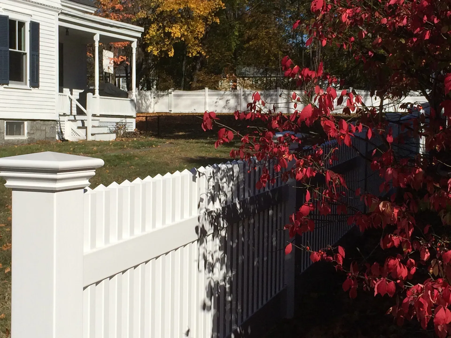 A white picket fence surrounds a house with red leaves