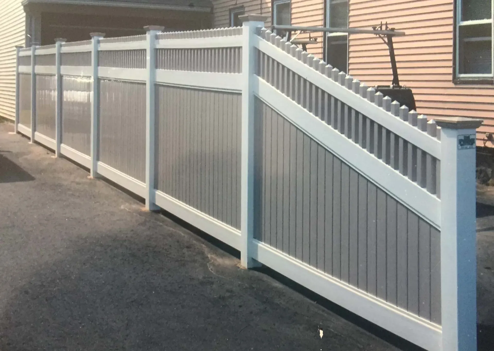 A gray and white fence along a driveway in front of a house