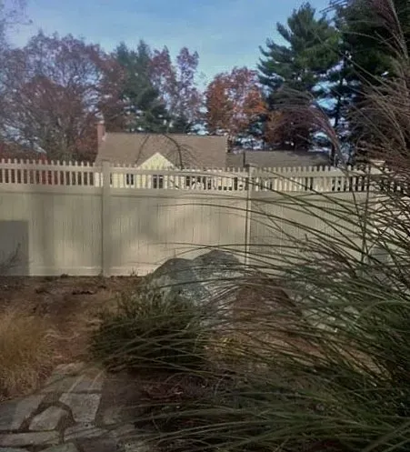 A white picket fence surrounds a backyard with trees in the background.
