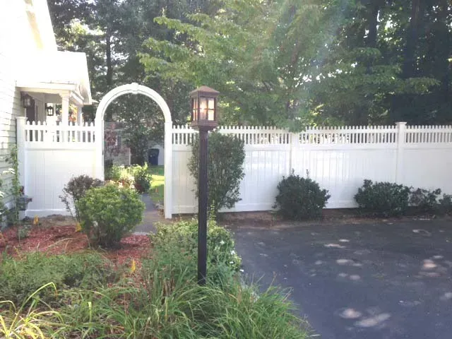 A white fence with a black lamp post in front of a house.
