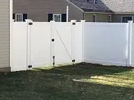 A white vinyl fence with a gate in the backyard of a house.