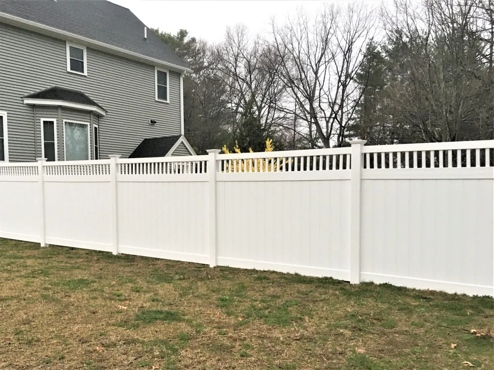 A white vinyl fence is in the backyard of a house.