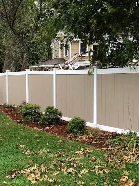 A tan and white fence surrounds a lush green yard in front of a house.