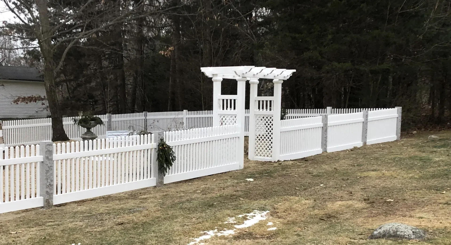 A white picket fence with a pergola in the middle of a yard.