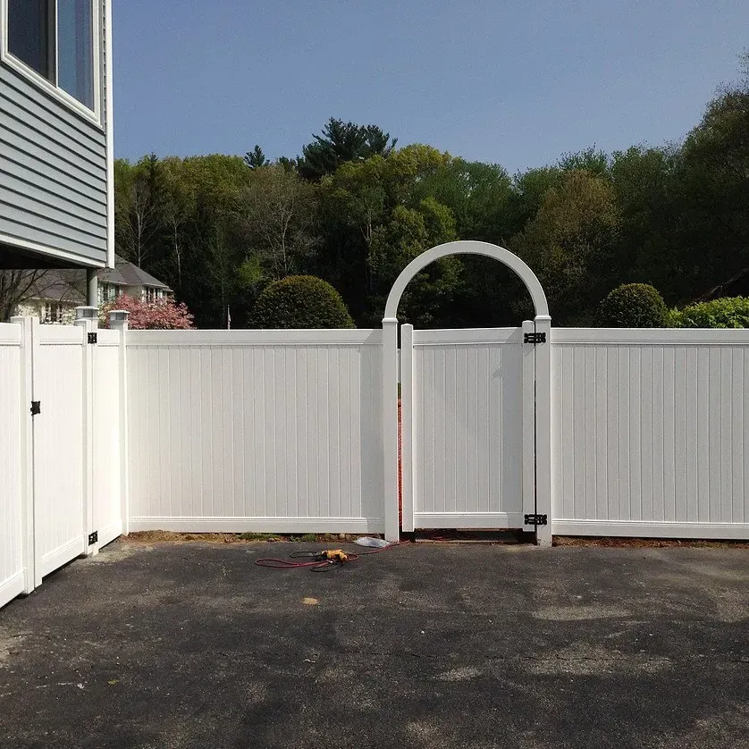 A white fence with an arched gate in front of a house
