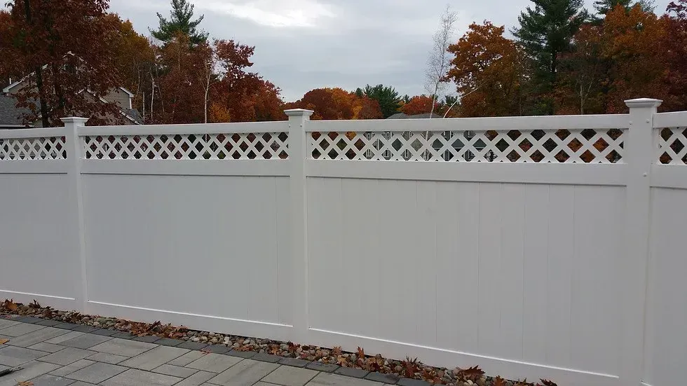 A white fence with a lattice design is surrounded by trees.
