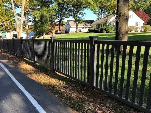 A wooden fence along the side of a road with a house in the background.