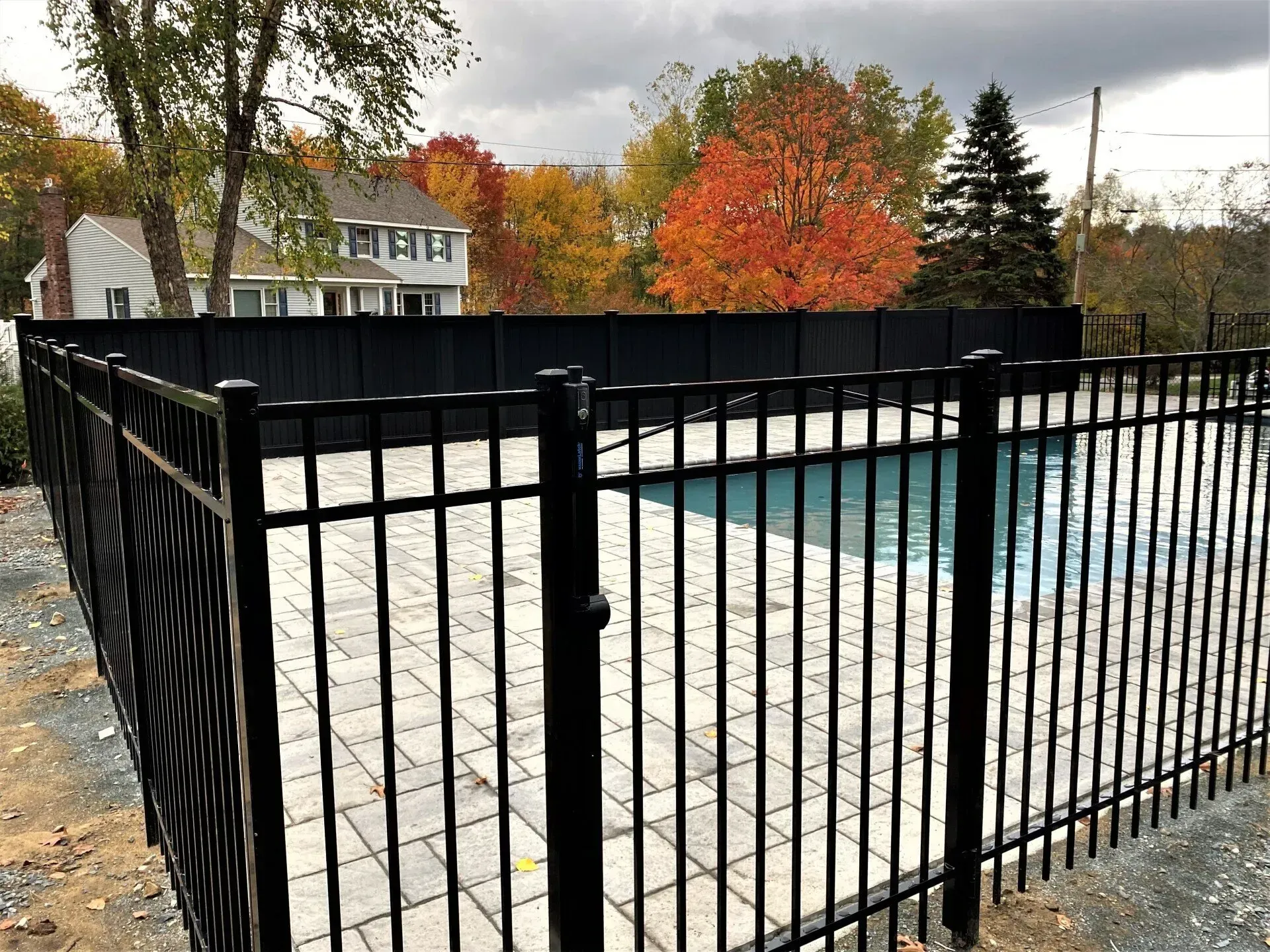 A black fence surrounds a swimming pool with a house in the background.