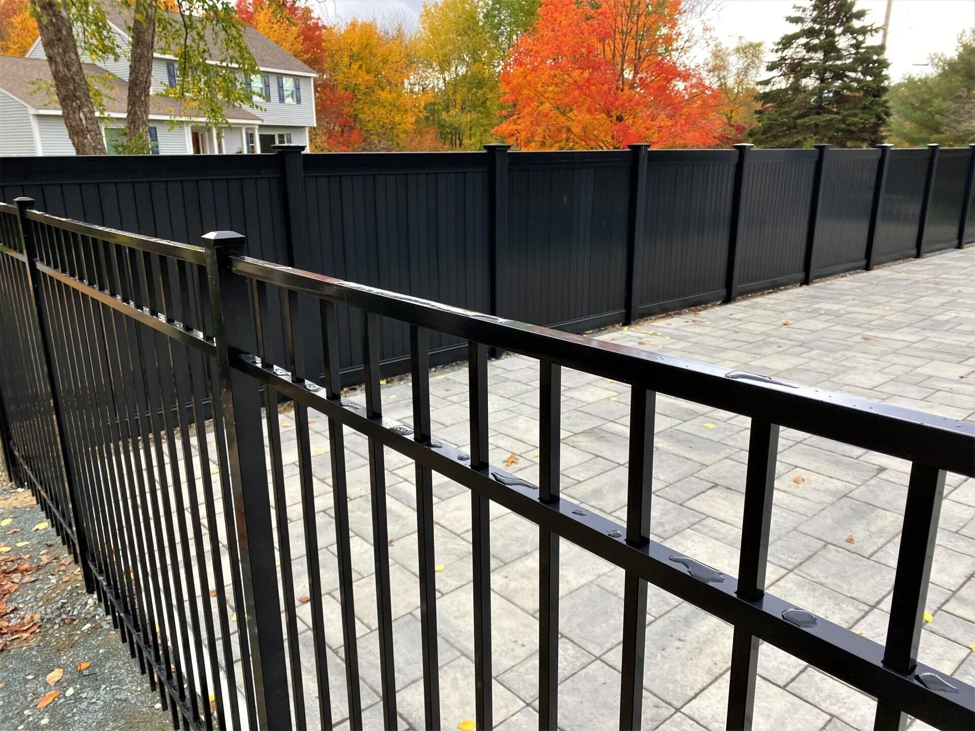 A black fence surrounds a patio with a house in the background.