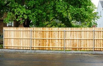 A wooden fence with a tree in the background and a house in the background.