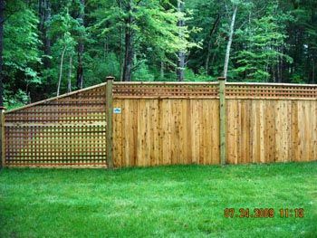 A wooden fence surrounds a lush green yard with trees in the background