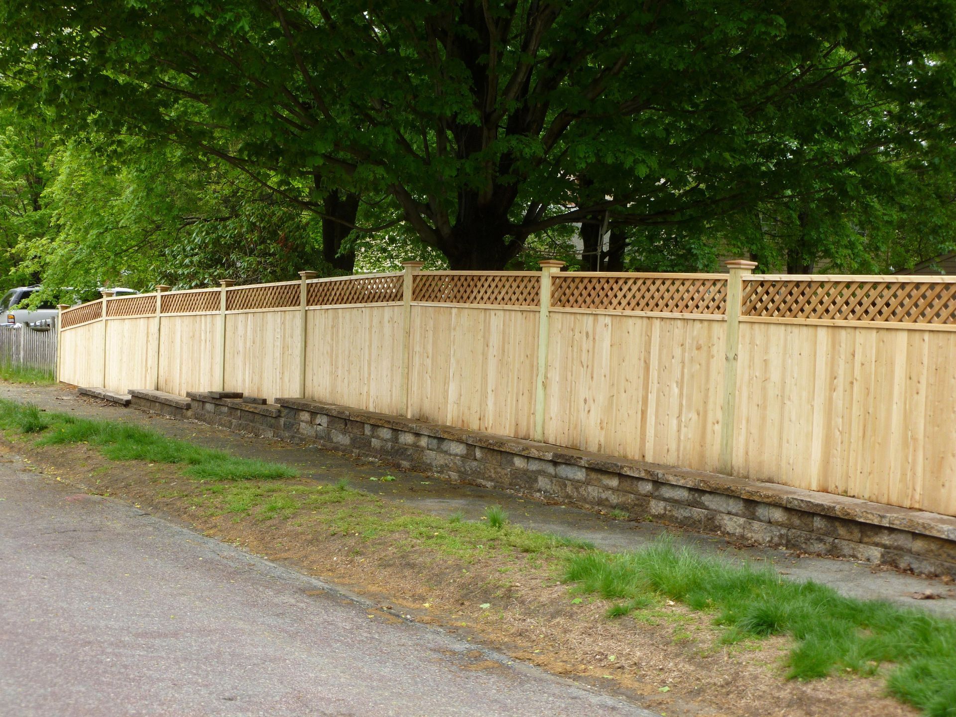 A wooden fence along the side of a road with trees in the background.