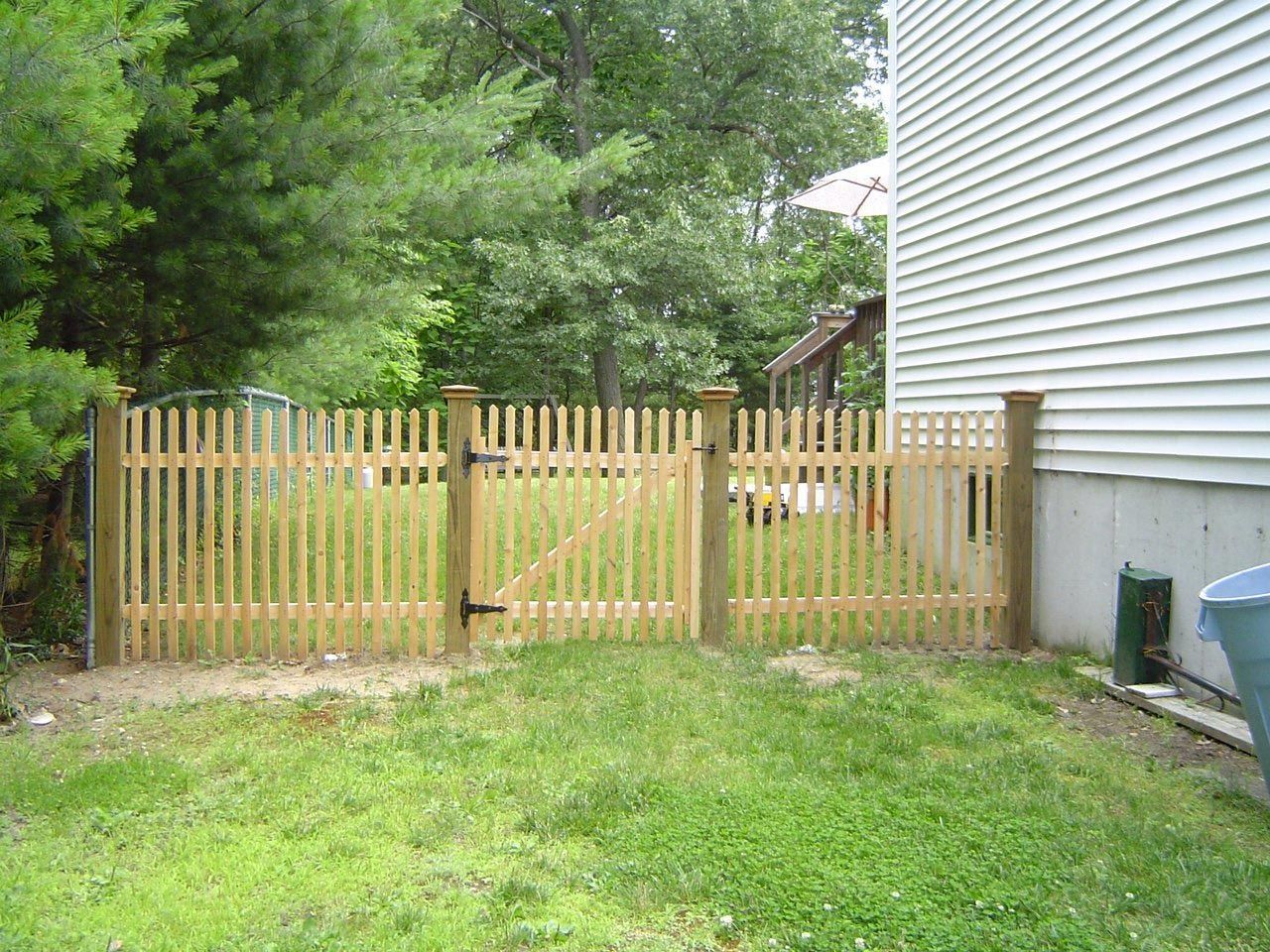 A wooden picket fence is in the backyard of a house.