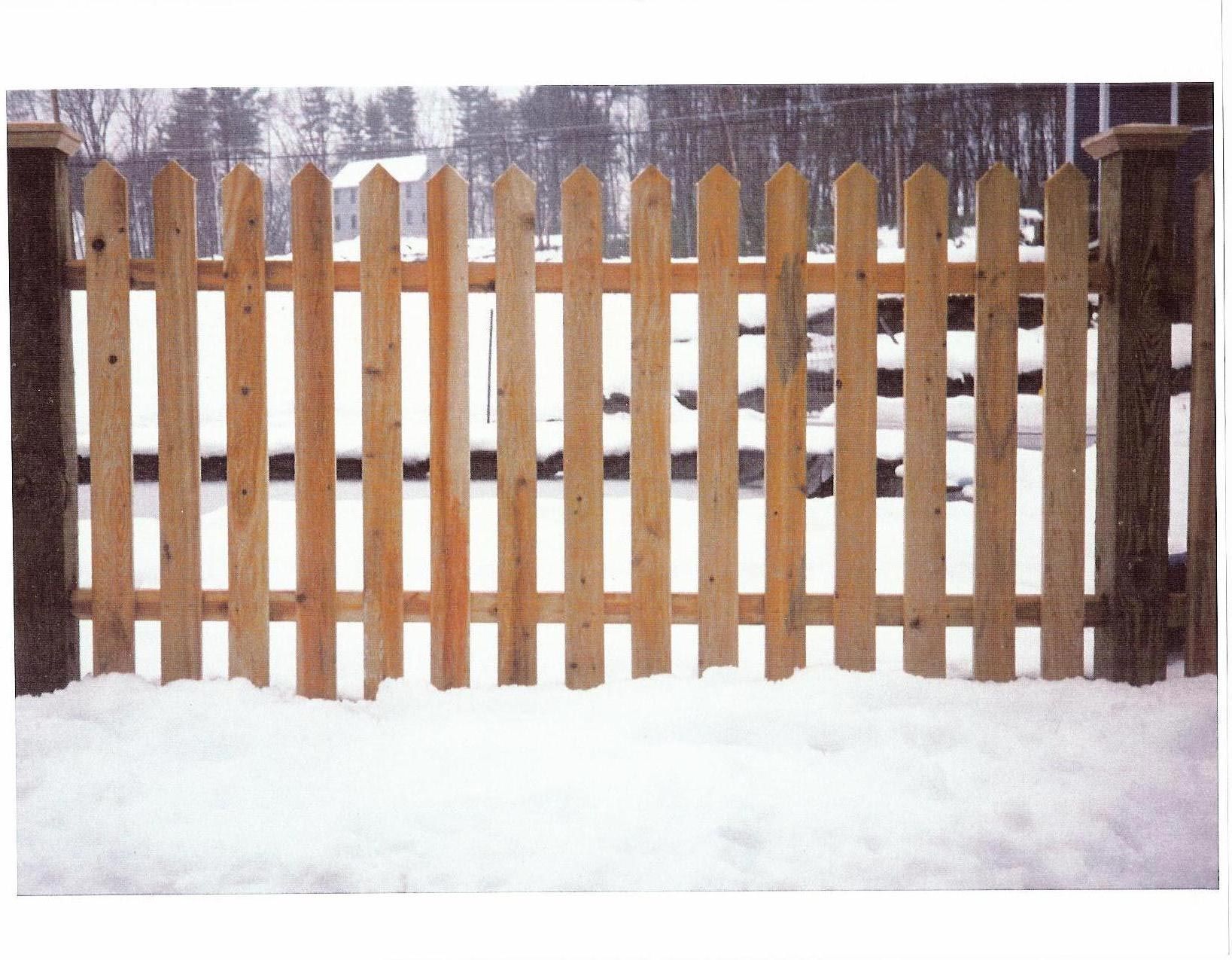 A wooden picket fence is surrounded by snow
