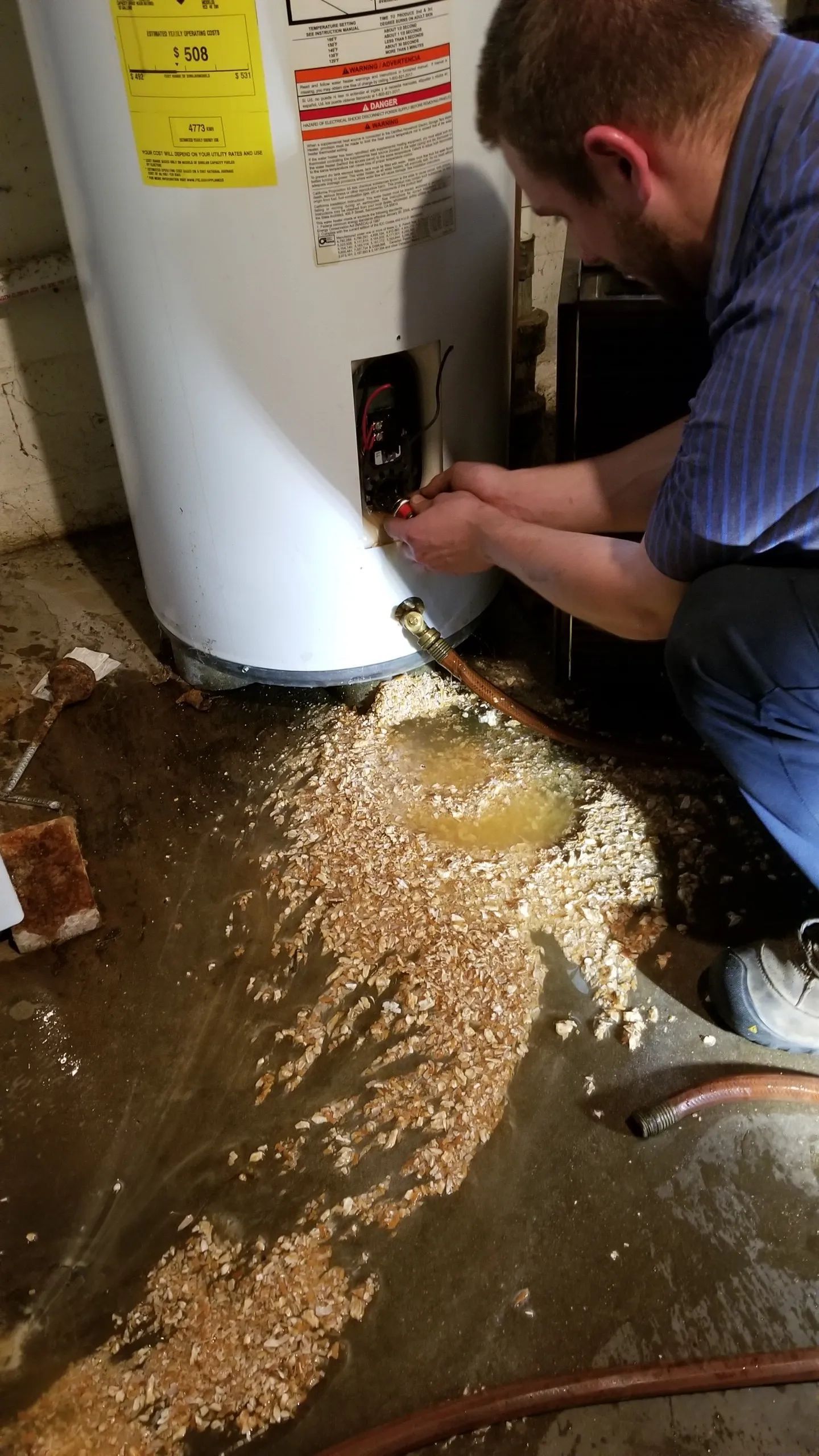 Person working on a water heater, water and wood chips on the floor.