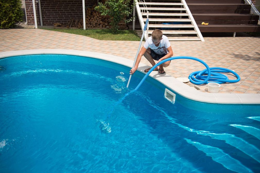 A man is cleaning a swimming pool with a hose.