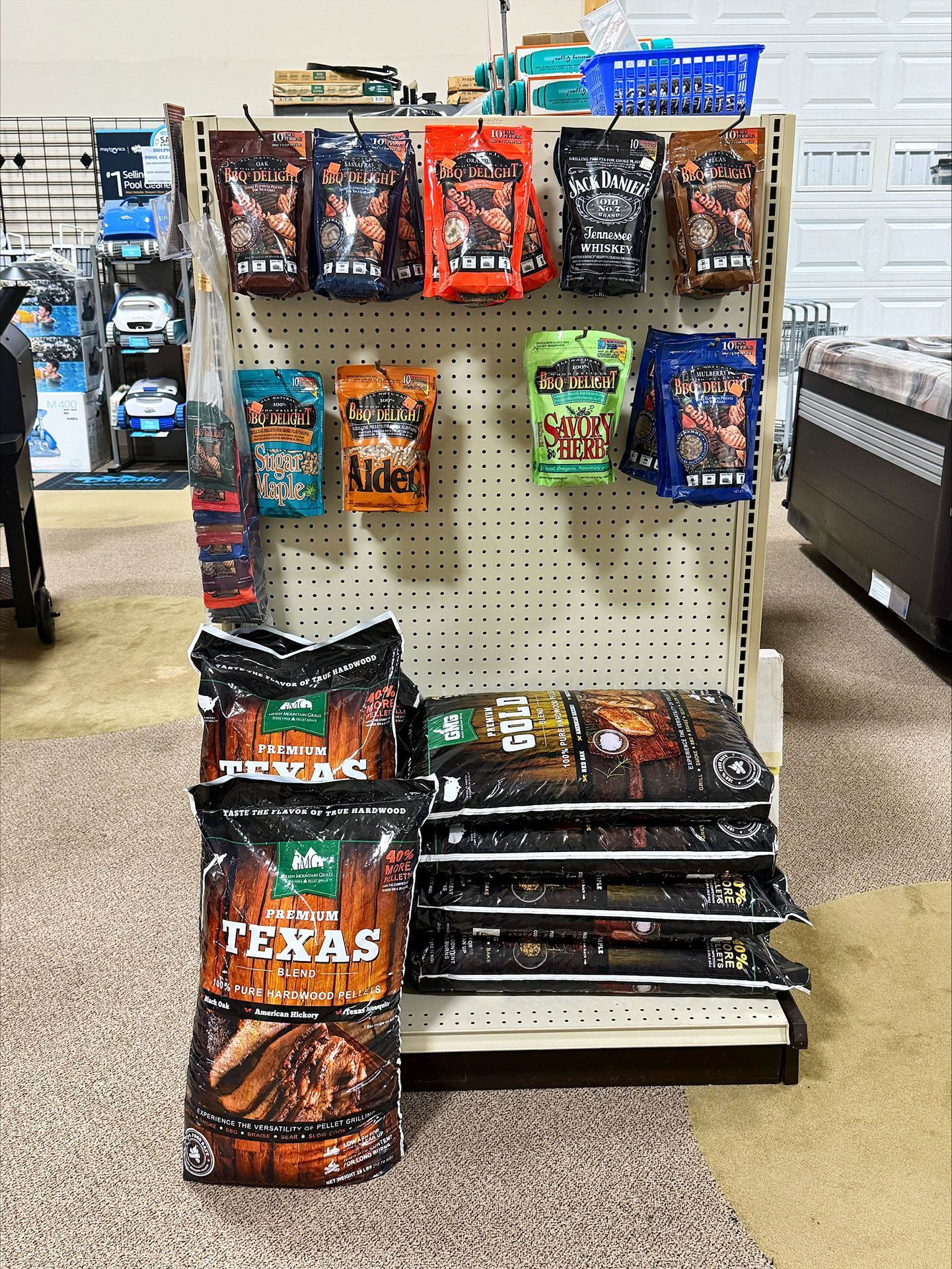 Display of bagged barbecue wood pellets in a store. Shelf holds various brands, colors, and types.