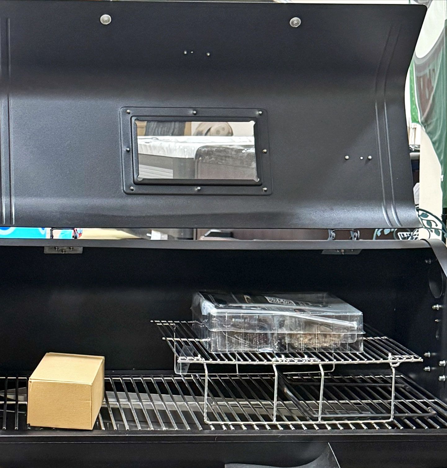 Open black grill interior with window, shelves, and a cardboard box.