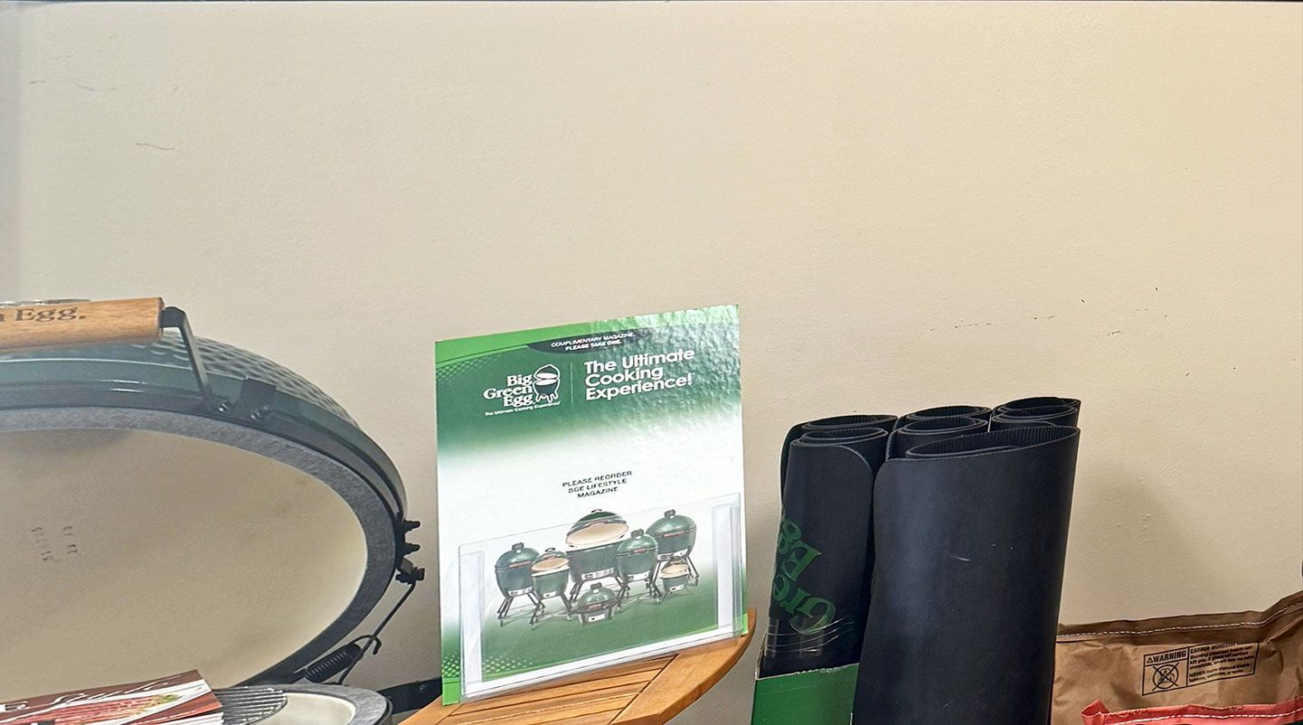 Green-covered book, black rolled-up items, and partially visible grill on a wooden surface against a light wall.